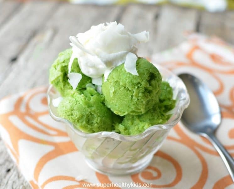 Green ice cream topped with coconut in a glass bowl